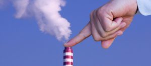 Mão de uma pessoa impedindo a saída de dióxido de carbono de uma indústria