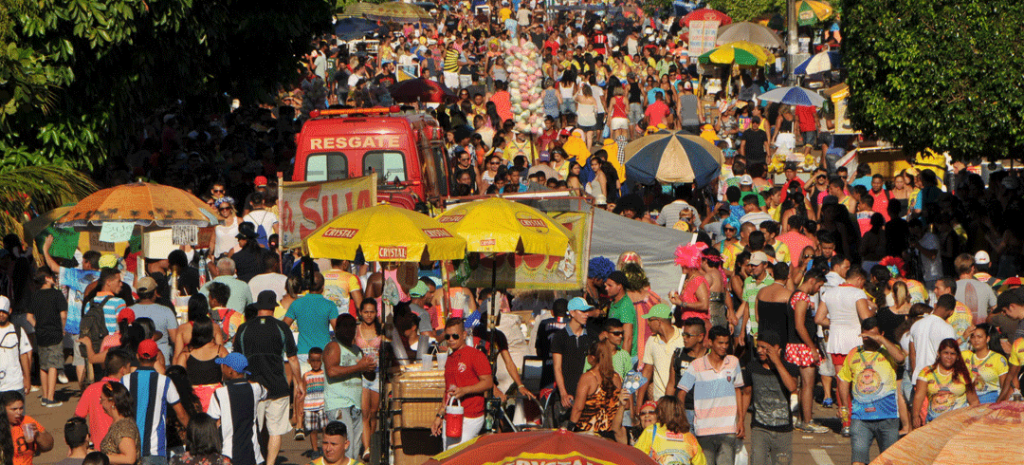 pessoas na rua com guarda sol amarelo e vendedores ambulantes durante festejo. 