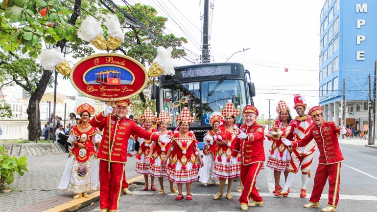 foliões vestidos de fantasia de carnaval vermelha na frente do ônibus do Expresso da Folia. 
