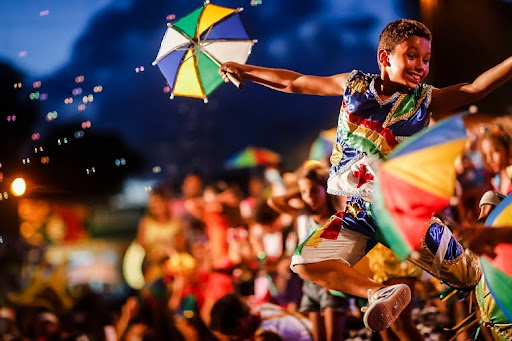menino com mini guarda-chuva e blusa com a bandeira de Pernambuco estampada em uma dança de frevo