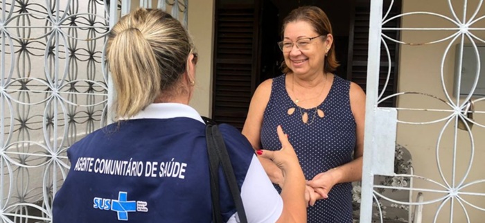 agente de saúde comunitária atendendo uma senhora branca de cabelos marrons e blusa azul marinho sem mangas