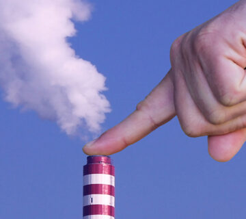 Mão de uma pessoa impedindo a saída de dióxido de carbono de uma indústria
